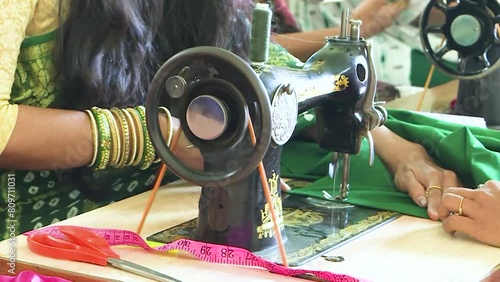 Indian woman working sewing machine - making homemade clothes,  closeup detail on moving needle and fingers holding fabric photo
