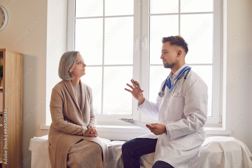 Portrait of elderly gray-haired woman in medical office listening to man doctor holding report file with appointment during medical exam in clinic. Health care and medicine concept. Portrait of elderly gray-haired woman in medical office listening to man doctor holding report file with appointment during medical exam in clinic. Health care and medicine concept.
