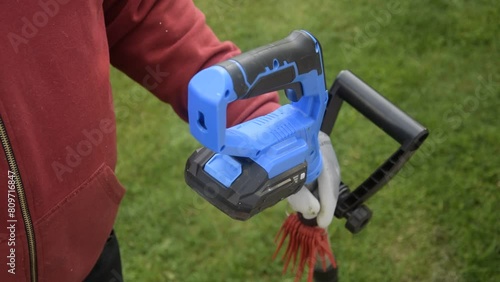 A man installs a battery in a cordless trimmer to mow the grass.