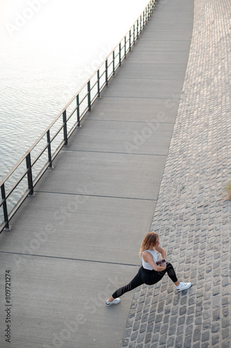 Beautiful woman in sport suit for fitness makes stretching exercises on the street. Young girl practicing sports outdoors. Concept of healthy lifestyle, sport, urban life