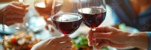 Close-up of hands clinking glasses in a toast with red wine at a social gathering