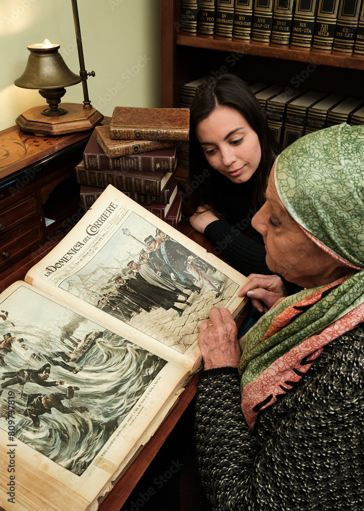 Foto scattata ad una nonna con sua nipote mentre leggono una raccolta di libri antichi.