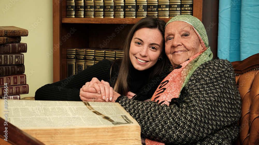 Foto scattata ad una nonna con sua nipote mentre leggono una raccolta di libri antichi.