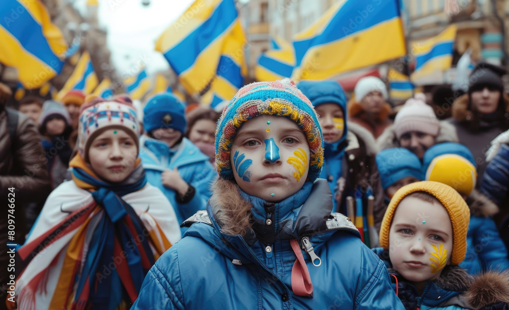 hildren with face painted in the colors of the Ukrainian flag, wrapped up and holding hands wearing a blue coat standing on a street lined with people cheering them
