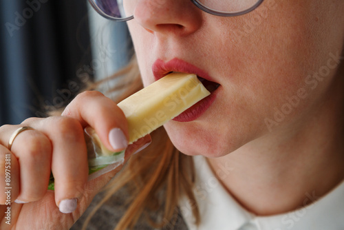 Close up of woman mouth eating a piece of holland cheese, healthy snack at lunchtime.