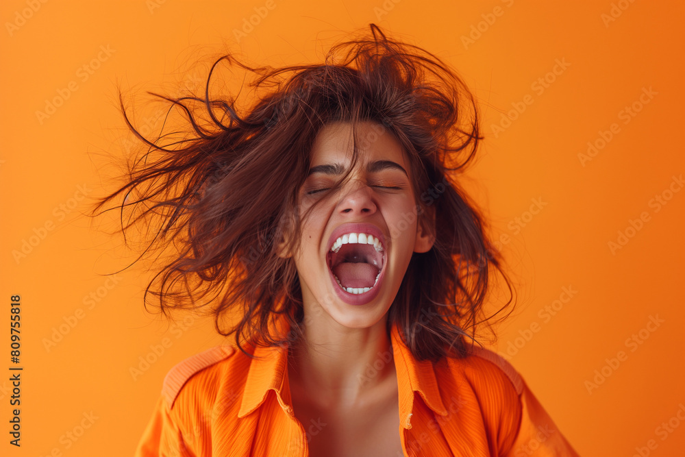 Portrait of an excited woman with an open mouth and messy hair screaming, isolated on an orange background, in the style of photo realistic photography