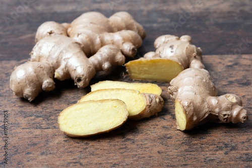 Fresh ginger root with cut slices on wooden background, close up,