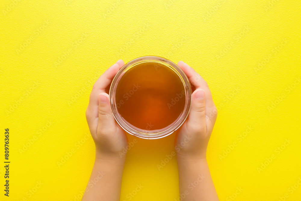Baby hands holding opened glass jar of fresh honey on bright yellow table background. Closeup. Point of view shot. Children sweet healthy food. Top down view. Baby hands holding opened glass jar of fresh honey on bright yellow table background. Closeup. Point of view shot. Children sweet healthy food. Top down view.
