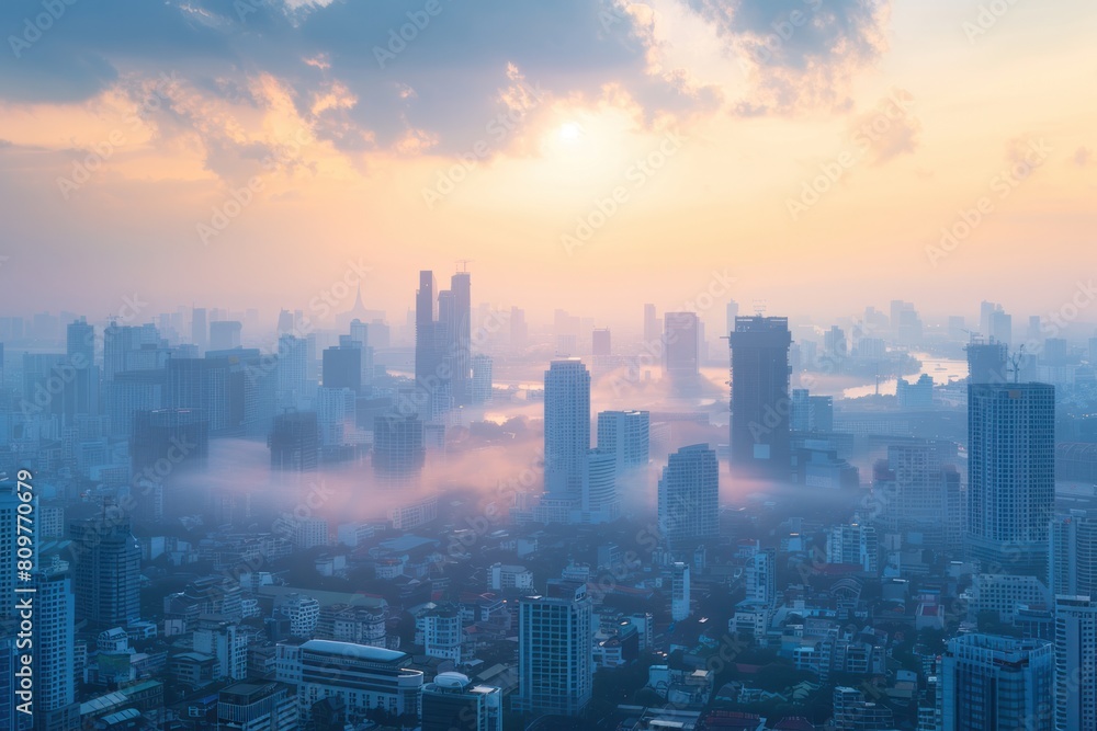 Fototapeta premium A city skyline with foggy clouds and a sun in the background. The city is covered in fog and the sun is barely visible