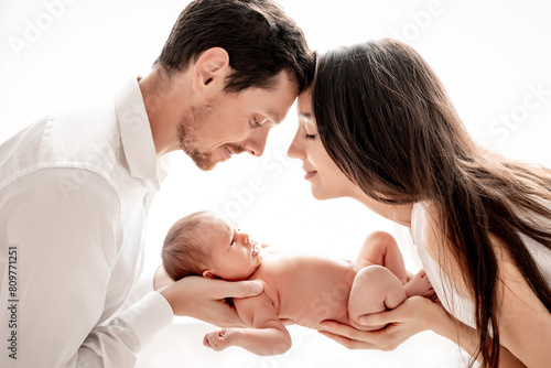 mom and dad with a newborn baby boy hugging and kissing gently holding him in their arms on a white isolated background of the window of the house, a happy family with a child