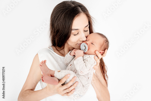 a mother with a newborn baby boy hugs and kisses gently holding him in her arms on a white isolated background of a house window