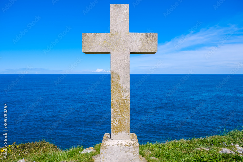 A Christian cross stands tall on a hill, casting a shadow against the backdrop of the vast ocean with waves crashing below. The scene exudes a sense of solemnity and reverence. A Christian cross stands tall on a hill, casting a shadow against the backdrop of the vast ocean with waves crashing below. The scene exudes a sense of solemnity and reverence.