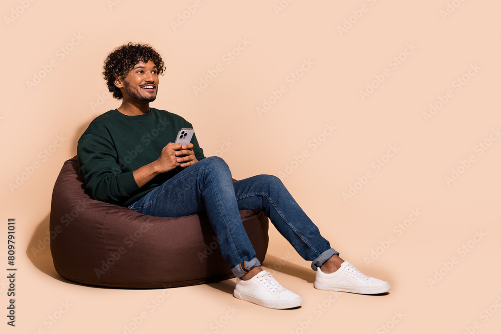 Full length photo of dreamy handsome guy wear sweatshirt texting modern gadget emtpy space isolated beige color background Full length photo of dreamy handsome guy wear sweatshirt texting modern gadget emtpy space isolated beige color background