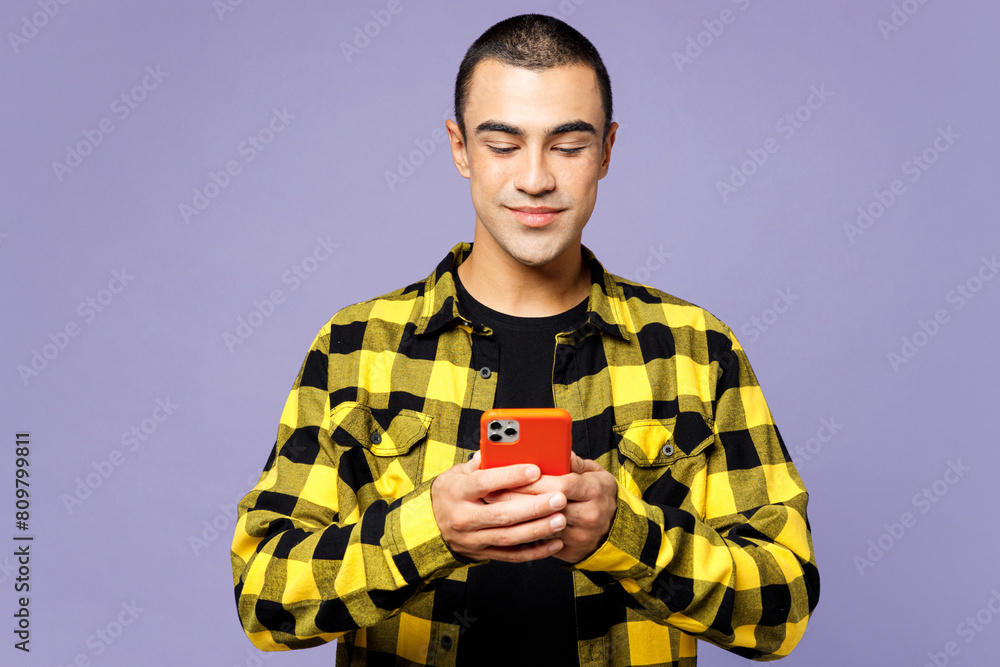 Young smiling middle eastern man wear yellow shirt casual clothes hold in hand use mobile cell phone chatting online isolated on plain pastel light purple background studio portrait Lifestyle concept Young smiling middle eastern man wear yellow shirt casual clothes hold in hand use mobile cell phone chatting online isolated on plain pastel light purple background studio portrait Lifestyle concept