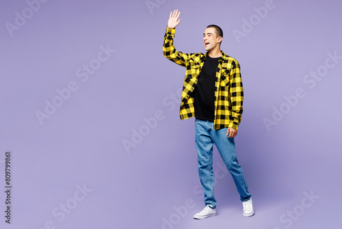 Full body side profile view young middle eastern man he wear yellow shirt casual clothes walking going waving hand isolated on plain pastel light purple background studio portrait. Lifestyle concept.