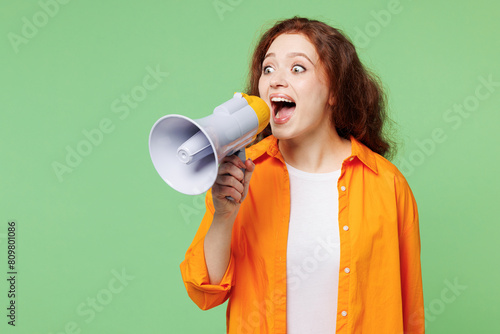 Young ginger woman wear orange shirt white t-shirt casual clothes hold in hand megaphone scream announces discounts sale Hurry up isolated on plain pastel light green background. Lifestyle concept.