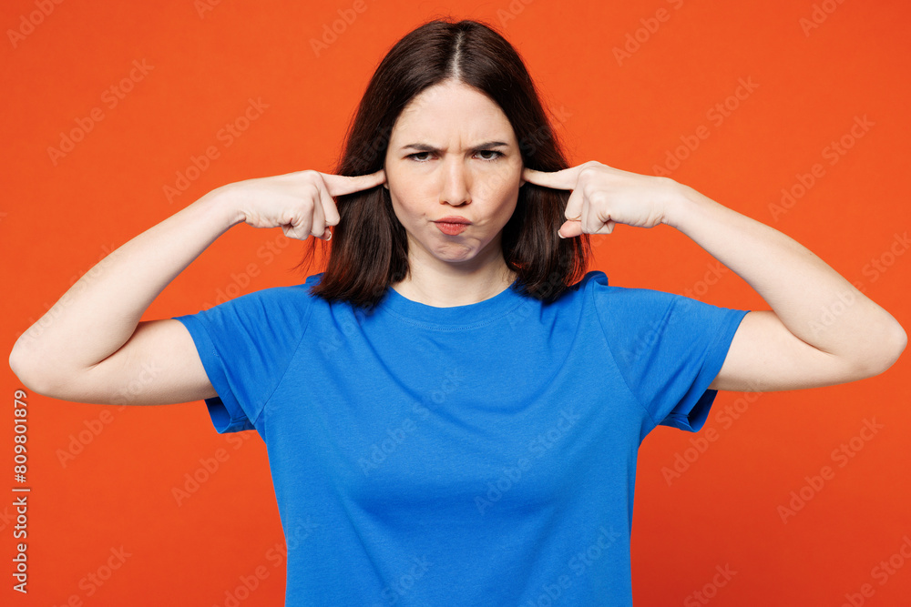 Young sad woman she wear blue t-shirt casual clothes cover ears with hands fingers do not want to listen scream look camera isolated on plain red orange background studio portrait. Lifestyle concept. Young sad woman she wear blue t-shirt casual clothes cover ears with hands fingers do not want to listen scream look camera isolated on plain red orange background studio portrait. Lifestyle concept.