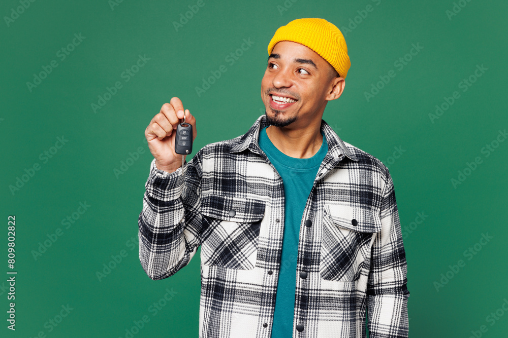 Young smiling happy man of African American ethnicity he wearing shirt blue t-shirt yellow hat hold car key fob keyless system look aside isolated on plain green background studio. Lifestyle concept.