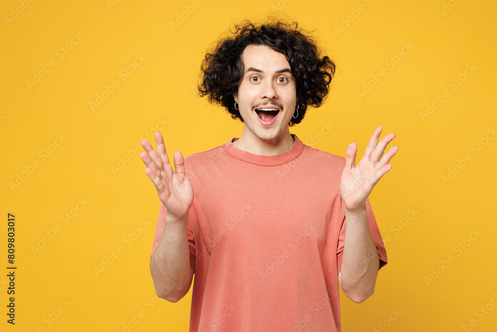 Young surprised shocked astonished overjoyed happy man he wearing pink t-shirt casual clothes looking camera spread hands isolated on plain yellow orange background studio portrait. Lifestyle concept. Young surprised shocked astonished overjoyed happy man he wearing pink t-shirt casual clothes looking camera spread hands isolated on plain yellow orange background studio portrait. Lifestyle concept.
