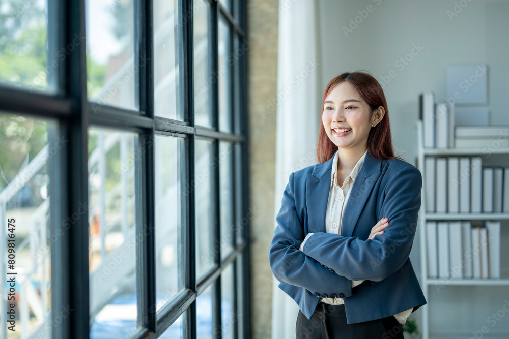 A woman in a blue jacket and white shirt stands in front of a window with her arms crossed. She has a smile on her face and she is confident and professional A woman in a blue jacket and white shirt stands in front of a window with her arms crossed. She has a smile on her face and she is confident and professional