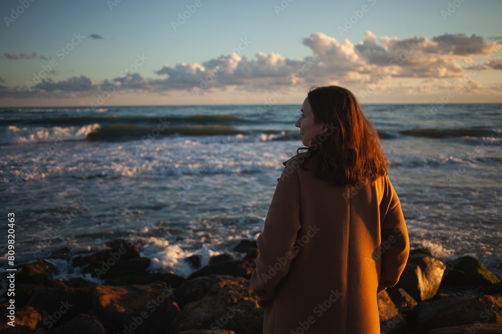 Woman enjoys sunset stroll by ocean.
