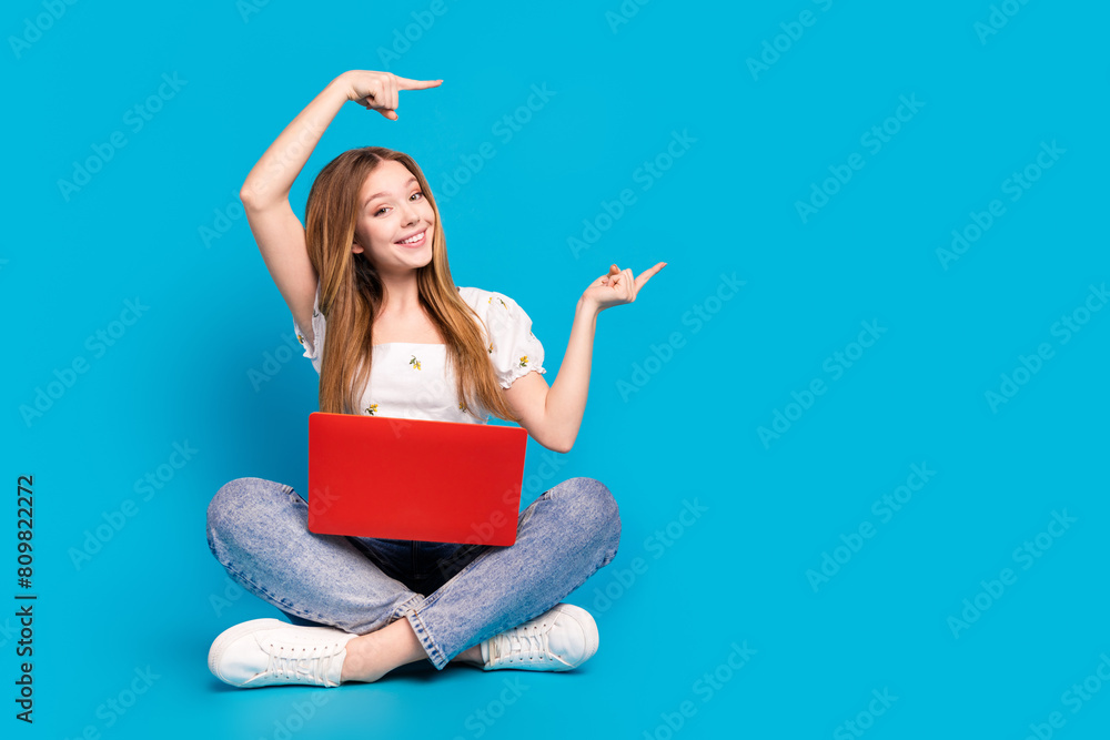 Full length portrait of lovely girl netbook direct fingers empty space wear top isolated on blue color background Full length portrait of lovely girl netbook direct fingers empty space wear top isolated on blue color background