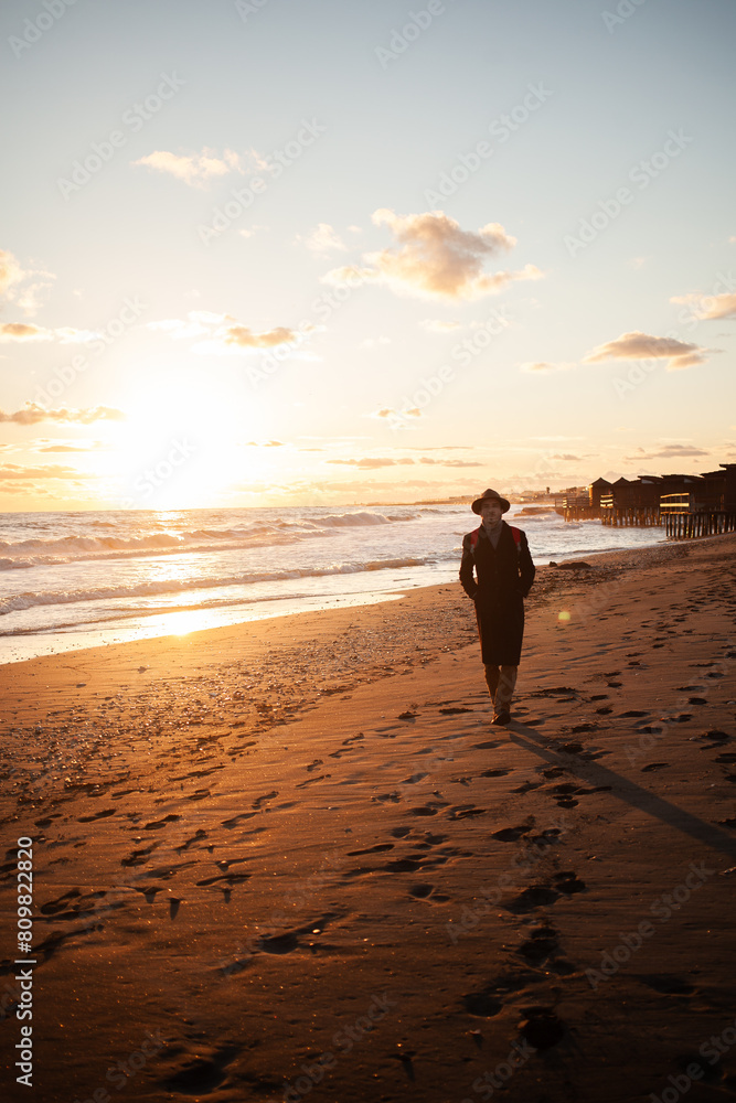 Naklejka premium Calm evening man walks by ocean under colorful sky.