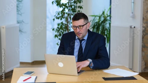  video. Caucasian man in black suit and glasses is working on the table at his computer, ooking at the screen, and filling pain in his neck.