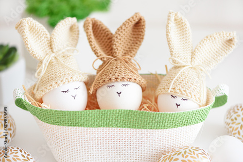 Easter eggs in crochet knitted hats with rabbit ears in nest. Easter celebration concept