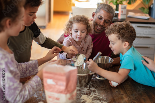 Family baking together in kitchen with father and children preparing dough photo