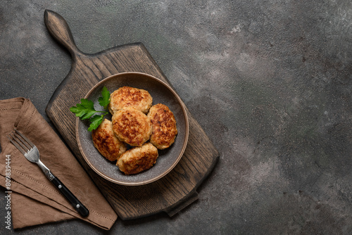 Fried meat cutlets in a bowl on a wooden cutting board, dark rustic background. Top view, flat lay, copy space.