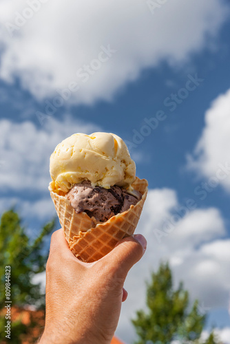 Eistüte mit Eiskugeln in der Hand vor blauem Himmel