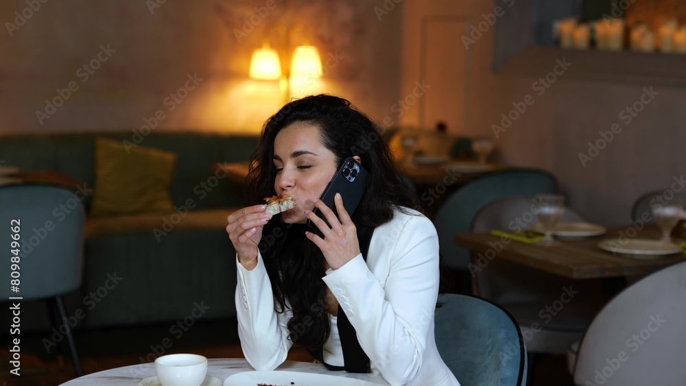 Happy pretty lady talking on mobile phone while biting bruschetta during lunch in modern restaurant. Copy space. Business, lifestyle concept. 