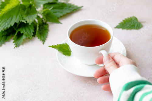 Herbal nettle tea with fresh nettle leaves. White cup of nettle tea on a table. Weight loss and detox. Alternative medicine. top view 
