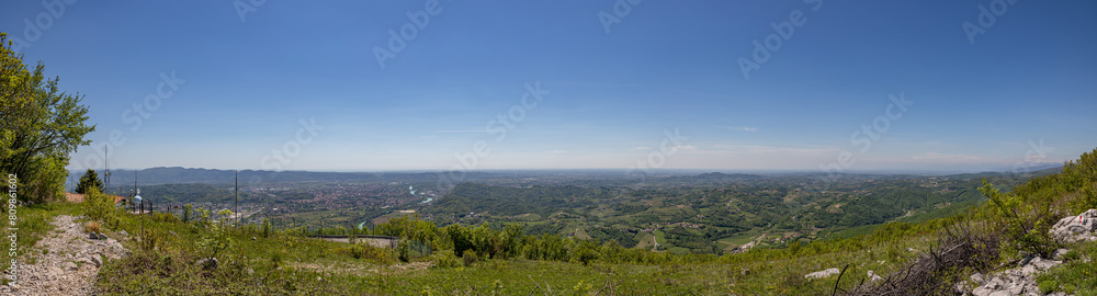 composizione panoramica con vista molto ampia, dal monte Sabotino, sull'area tra pianura e colline, tra l'Italia e la Slovenia, mista urbana e naturale, durante una bellissima giornata estiva