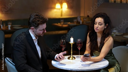 Happy young man and woman talking while looking at phone screen, having date in the restaurant. Lifestyle, love, relationships concept. 