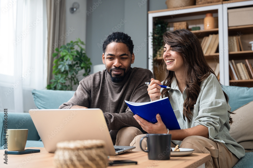 Positive hipster couple having fun while working together remotely at home using modern technology, cheerful young business male and female laughing. Businesspeople in home office Independence concept
