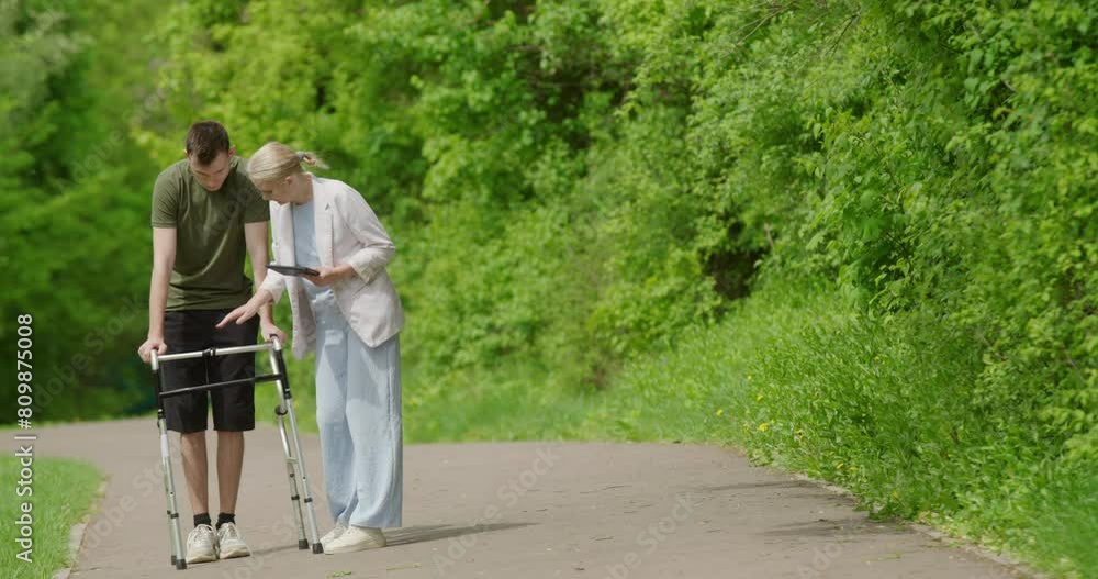A health worker helps in the rehabilitation of a young man, teaches him to use a walker.