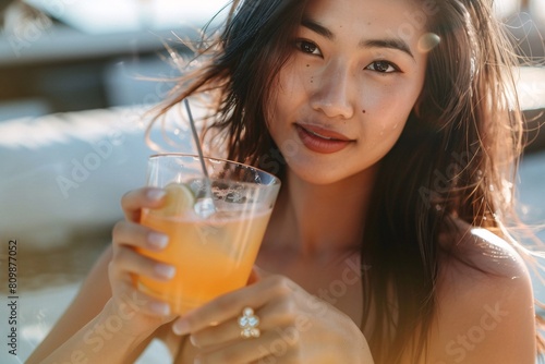 An up-close view of an Asian woman with bronzed skin, slender yet shapely, enjoying a cocktail in a bikini
