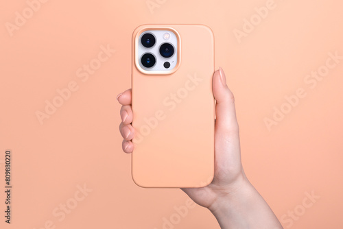 Smartphone in female hand in fuzz peach silicone cover isolated on 2024 color of the year background phone case mock up in monochrome colours back view