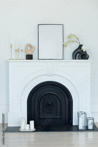 White modern decorated fireplace and mantel in interior design Scandi living room. Stylish room decorated with vase with flowers, vintage metal candlesticks with candles, picture on fireplace shelf