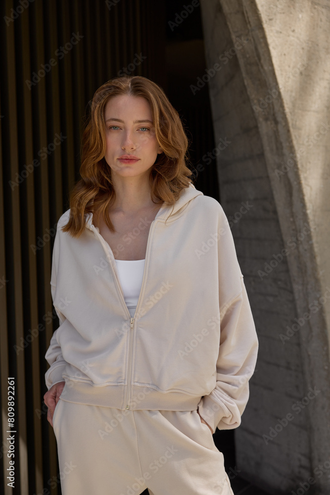 Portrait of a young woman in casual beige tracksuit standing near a building