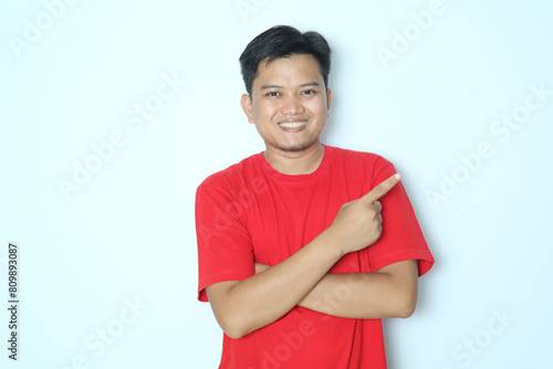 Young Asian man pointing finger to the left with smiling face. Wearing red t-shirt photo