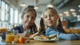 Two cute ten years old girls sitting at the table in school cafeteria. Young students having food during lunch break in dining hall. copy space for text.