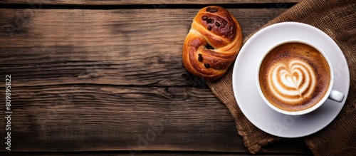 A top down view of a cup of coffee or cappuccino alongside a plate of traditional Swedish cinnamon buns known as kanelbulle The image is set against a wooden background offering ample copy space photo