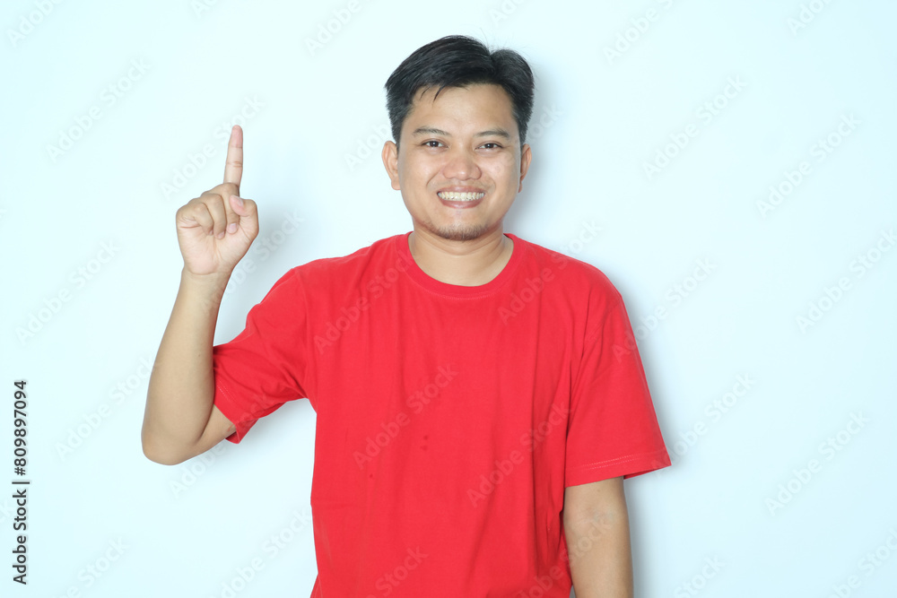 Young Asian man smiling happy and pointing finger right hands up. Wearing red t-shirt Young Asian man smiling happy and pointing finger right hands up. Wearing red t-shirt