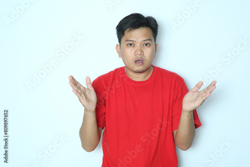 Young Asian man looks at the camera with a confused expression. Wearing red t-shirt photo