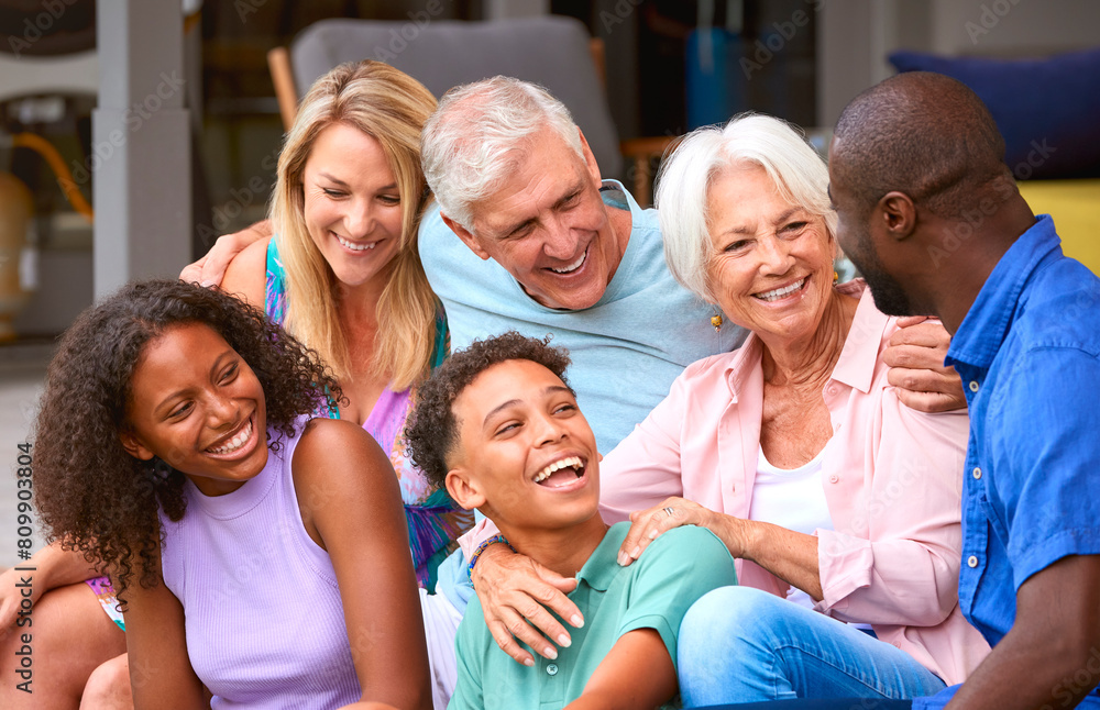 Three Generation Family Laughing And Smiling Sitting Outdoors At Home On Deck Together