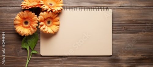 Top view copy space image of three gerbera flowers and a blank paged notebook resting on a wooden table