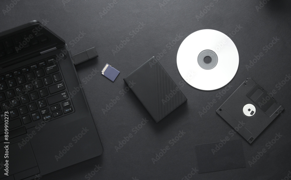 Outdated and modern digital storage media with laptop on black background Outdated and modern digital storage media with laptop on black background